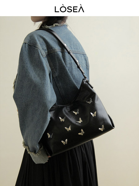 Black shoulder bag with butterfly embellishments worn by a model