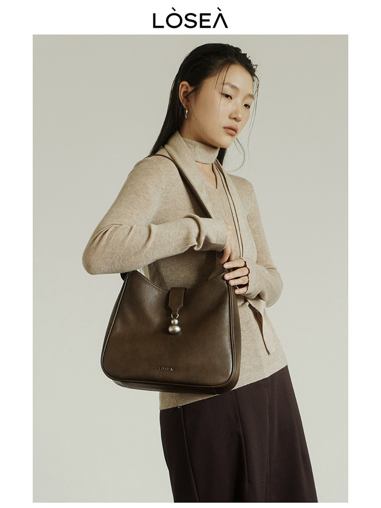 Brown leather shoulder bag worn by a model with a beige turtleneck sweater