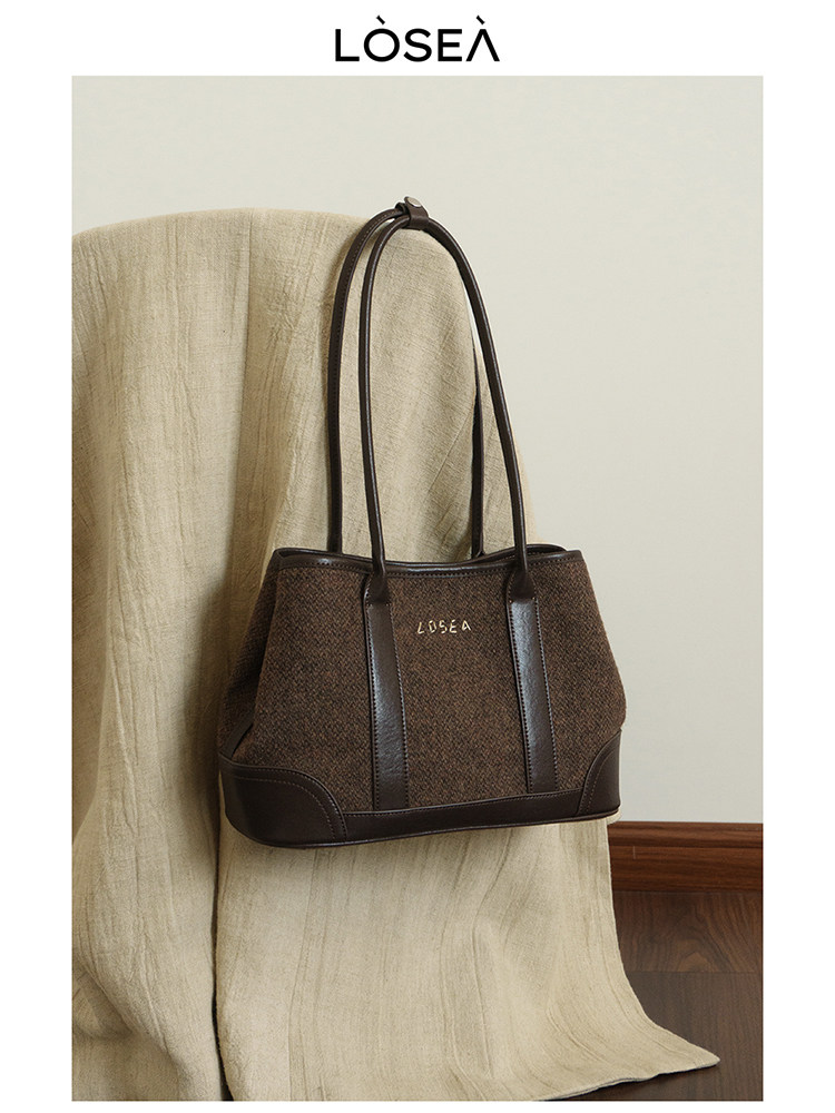 Brown textured tote handbag with dark leather trim and long handles on a chair