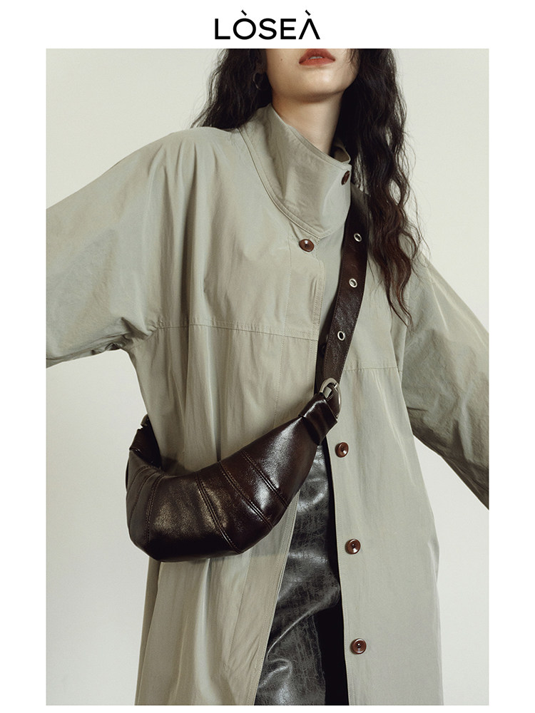 Model wearing a beige long coat with a dark brown leather crossbody bag