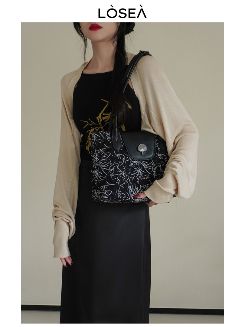 Black patterned handbag worn by a model with a beige cardigan and black dress