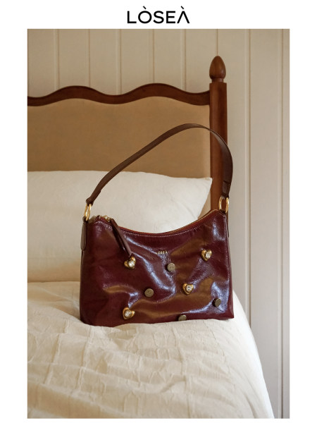Burgundy leather shoulder handbag with gold hardware on a bed