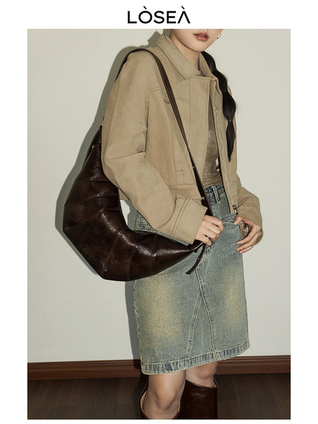 Model wearing a beige jacket and denim skirt with a dark brown shoulder bag