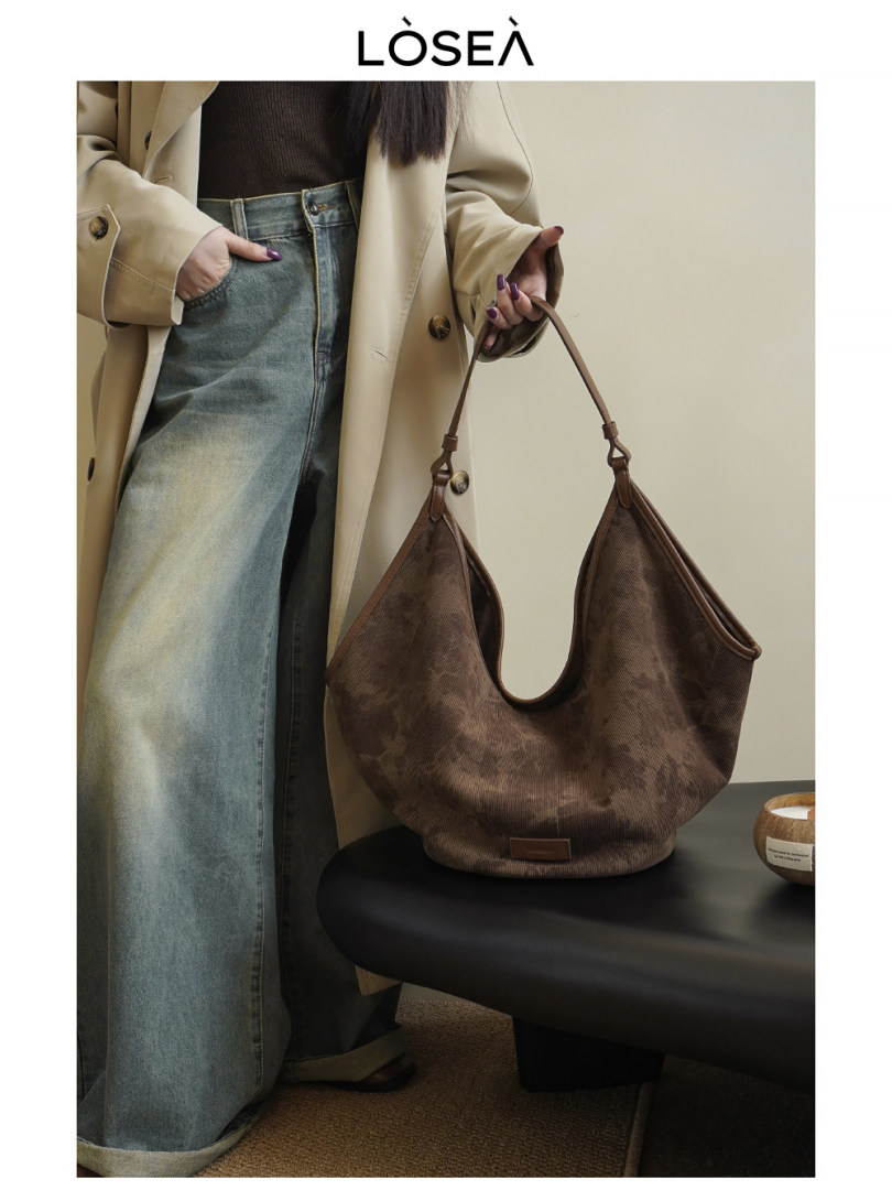 Brown suede hobo handbag held by a woman in a beige coat and jeans