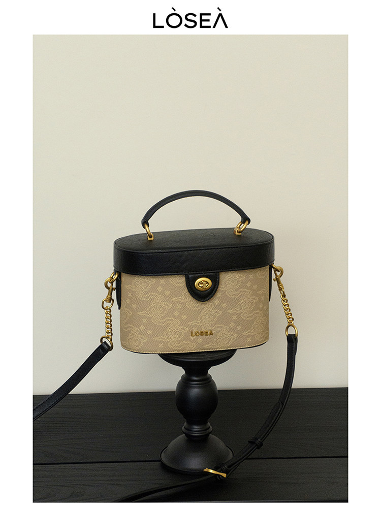 Black and beige structured handbag with gold chain strap on display stand