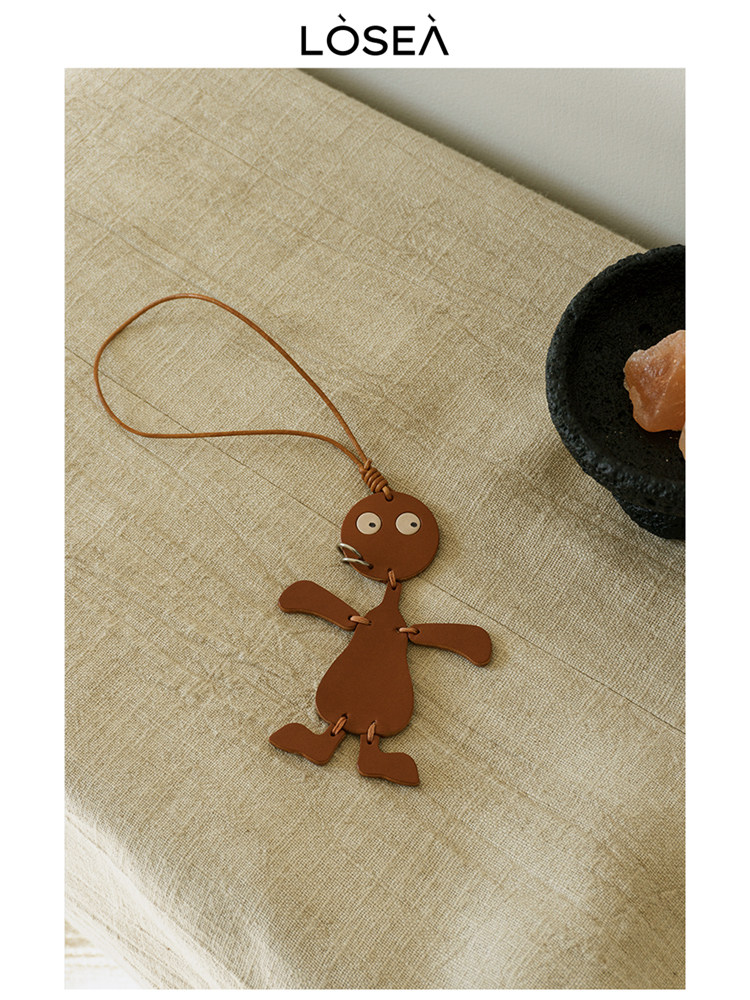 Brown leather character keychain with loop strap on a textured fabric surface