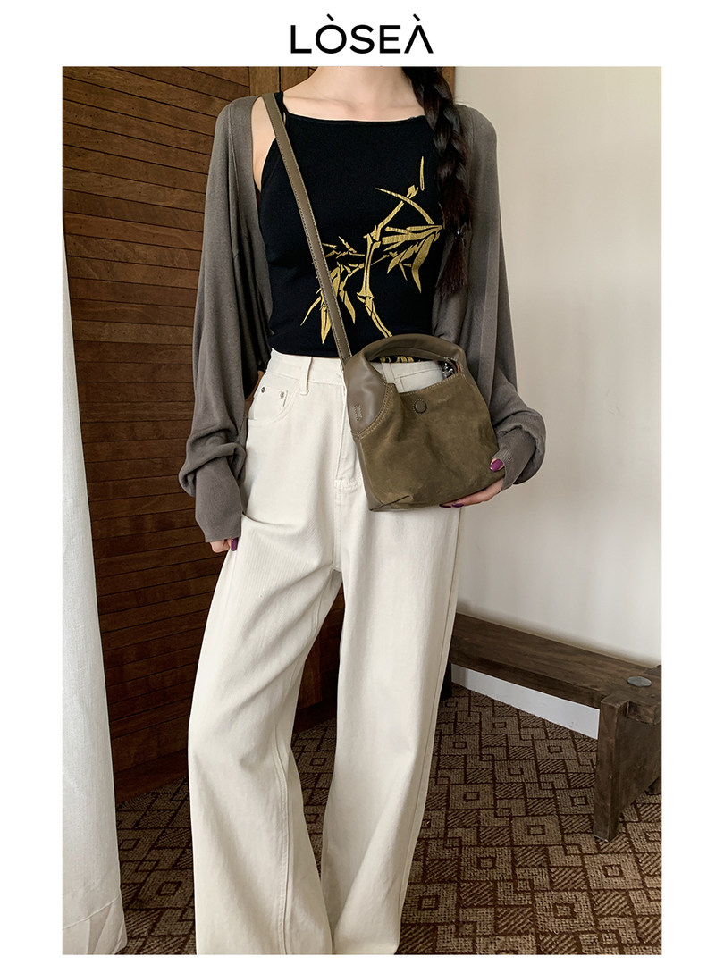 Model wearing a black graphic top with a gray cardigan, white wide-leg pants, and a brown crossbody bag