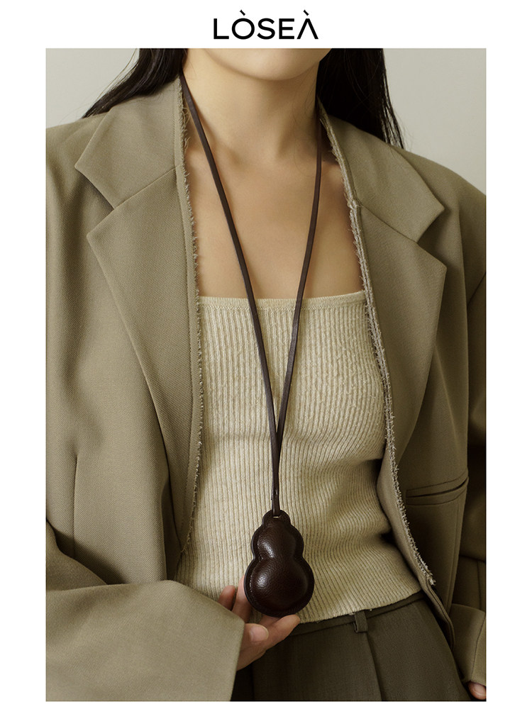 Model wearing a beige blazer over a ribbed knit top with a pendant necklace