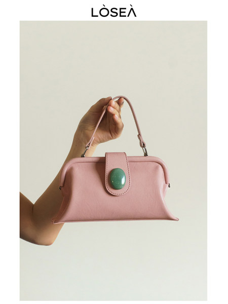 Pink handbag with a green clasp and top handle being held by a hand