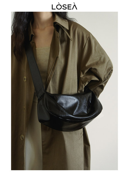 Black leather shoulder bag worn by a model with an oversized coat