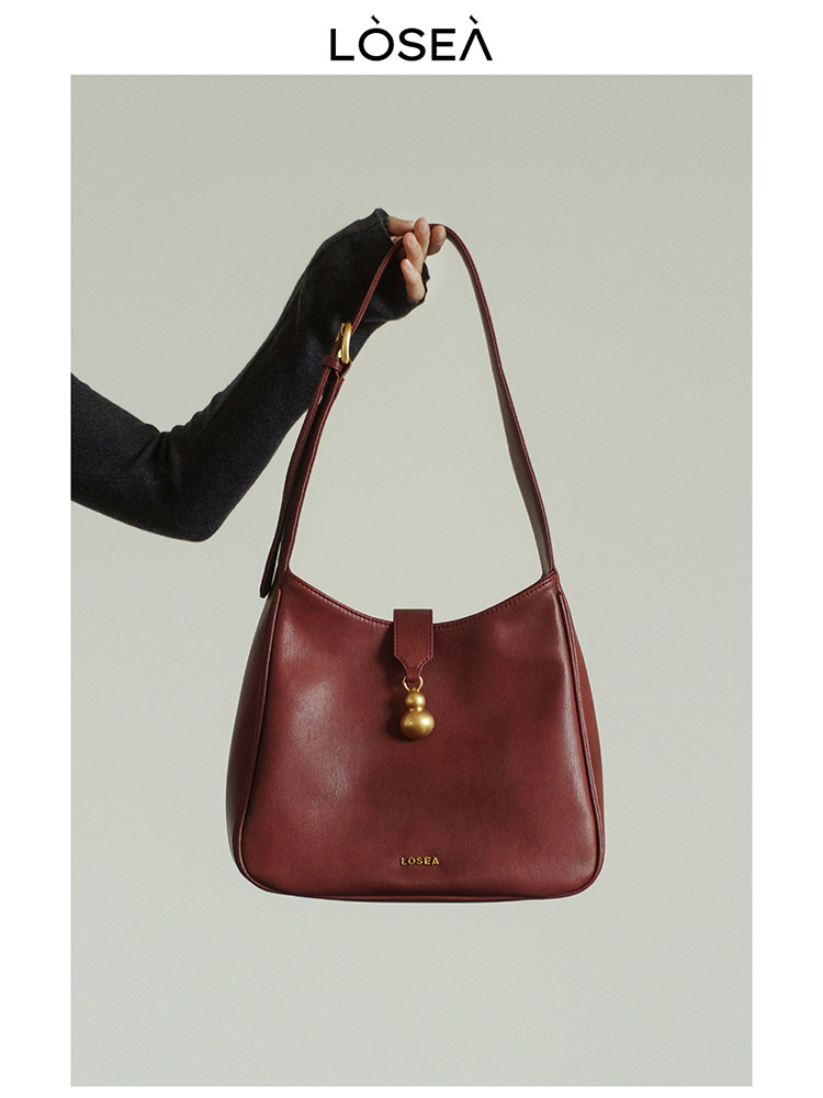 Burgundy leather shoulder handbag with gold charm detail on a model's arm