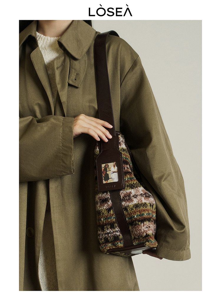 Model wearing an olive coat and holding a textured brown shoulder bag
