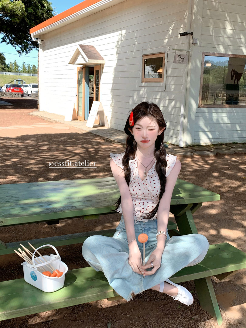 Woman wearing a sleeveless patterned top with light blue jeans outdoors