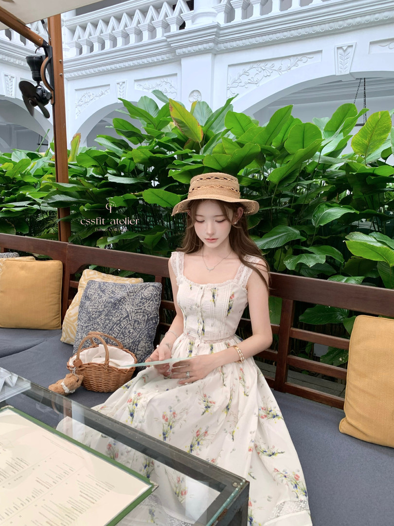 Woman wearing a light floral sleeveless dress and straw hat seated in a garden setting