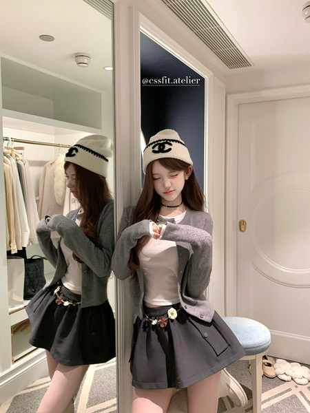 Young woman wearing a gray cardigan, white top, black mini skirt, and knit beanie in a mirror selfie