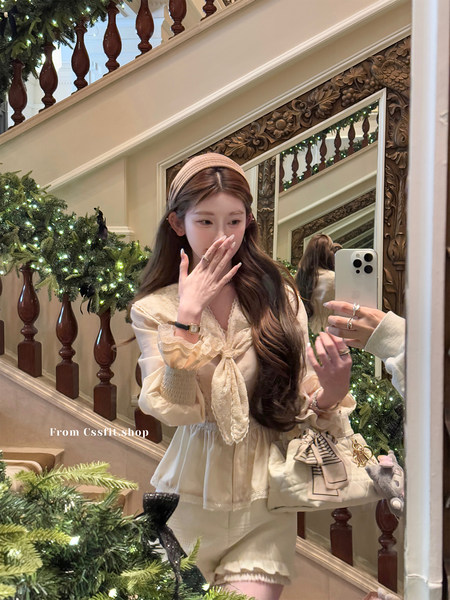 Woman wearing a cream lace blouse and matching skirt with a small bow handbag in a festive interior