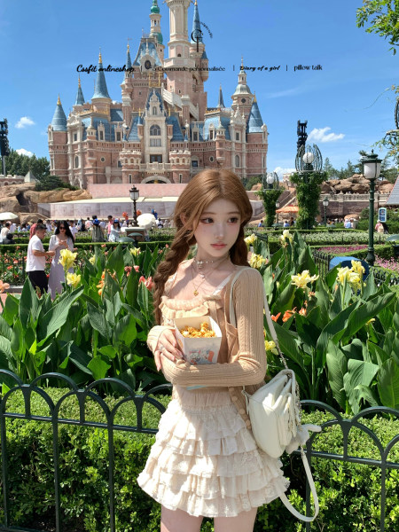 Model wearing a cream layered dress and cardigan at a theme park