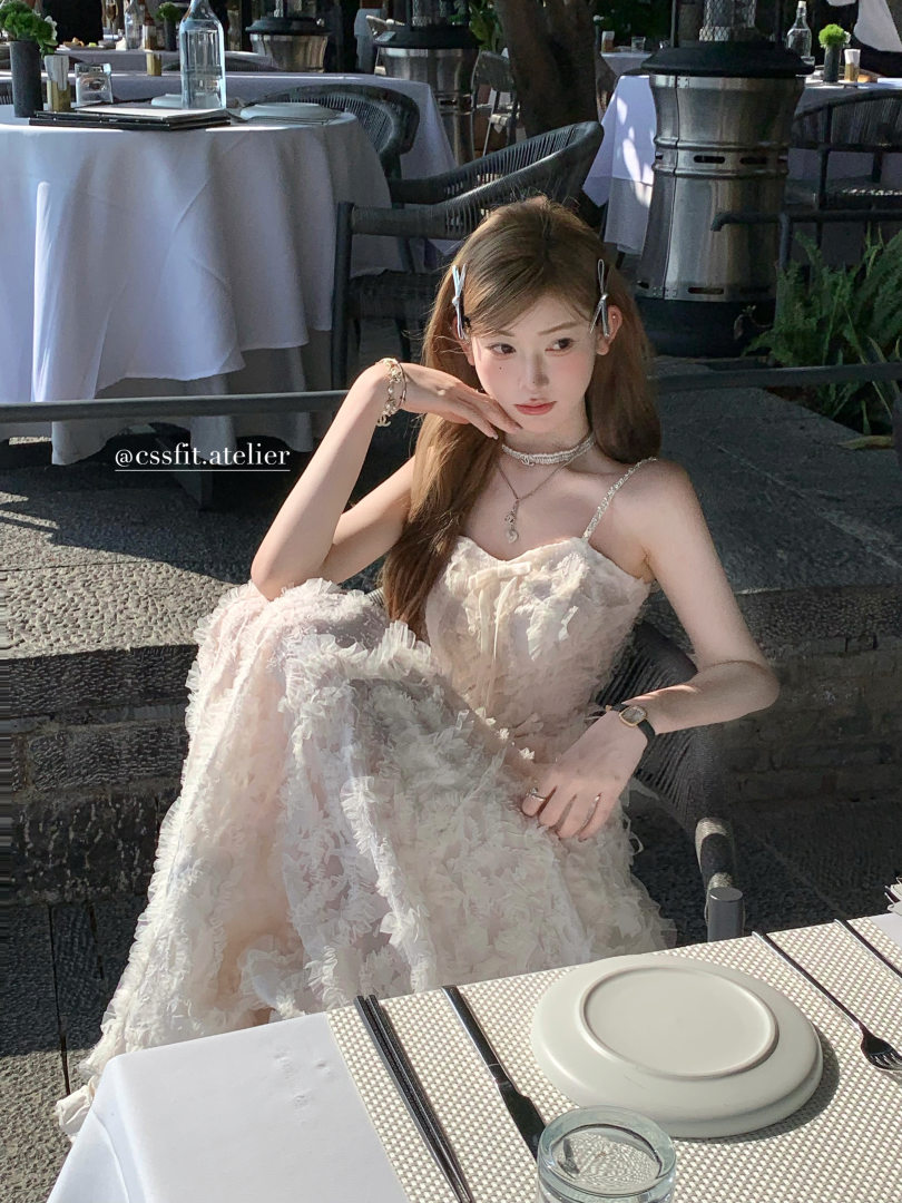 Model wearing a light pink floral strap dress seated at a restaurant table