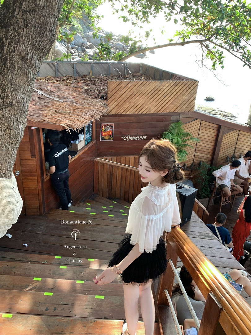 Woman wearing a white sheer blouse and black skirt outdoors on a wooden deck