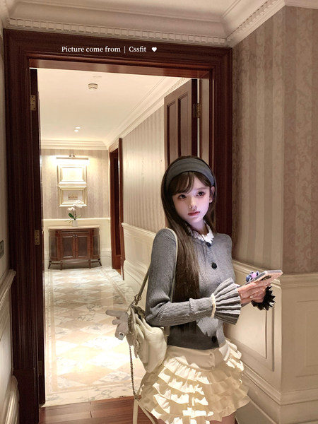 Woman modeling a gray cardigan and cream ruffled skirt indoors