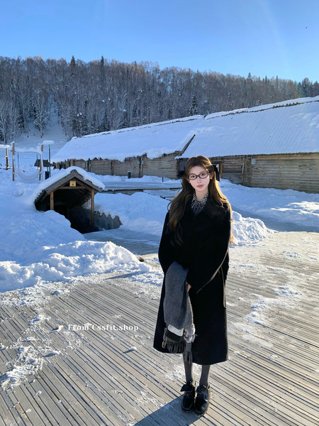 Woman wearing a long black winter coat with scarf and glasses outdoors in a snowy landscape