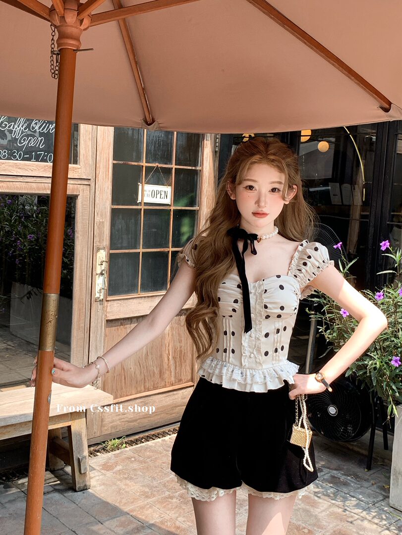 Model wearing a white polka dot ruffled top with black shorts at an outdoor cafe