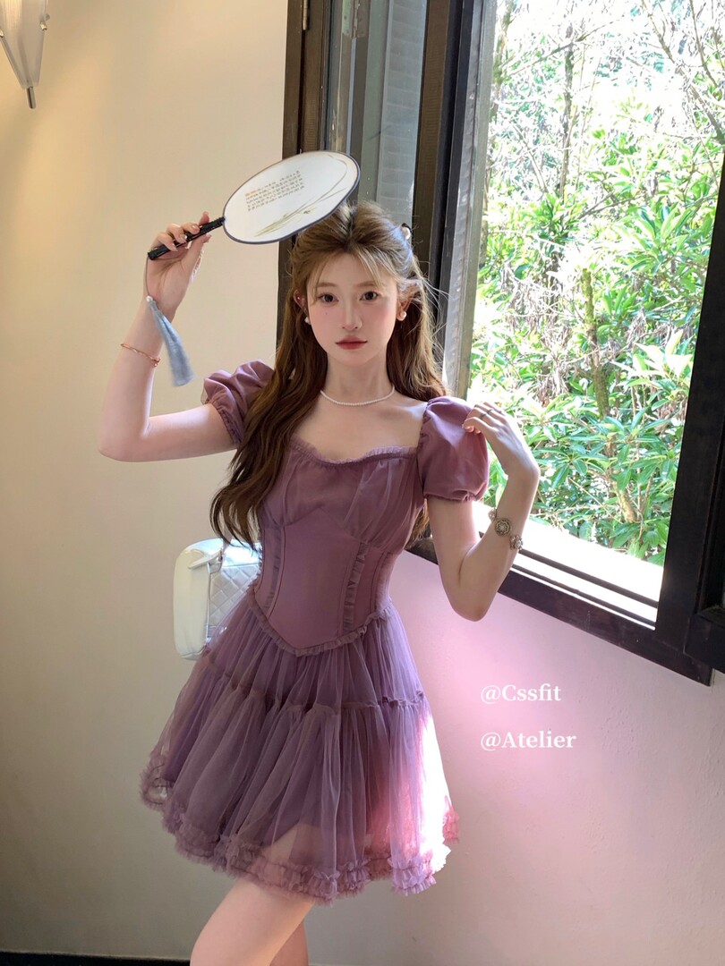 Woman wearing a purple puff-sleeve tulle dress indoors by a window