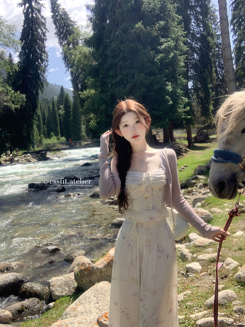 Woman wearing a light floral dress with a cardigan by a river in a forest setting