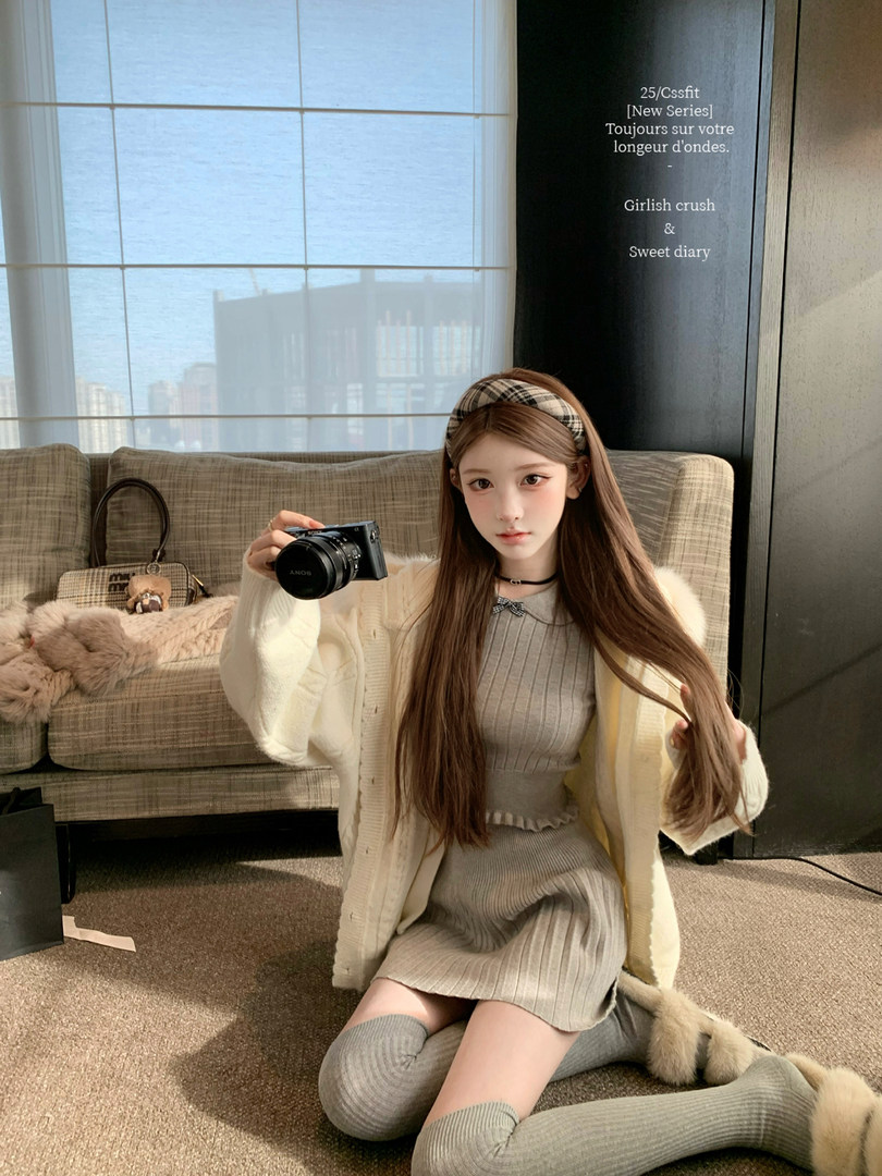 Model wearing a cream knit cardigan and ribbed dress with matching leg warmers, holding a camera indoors