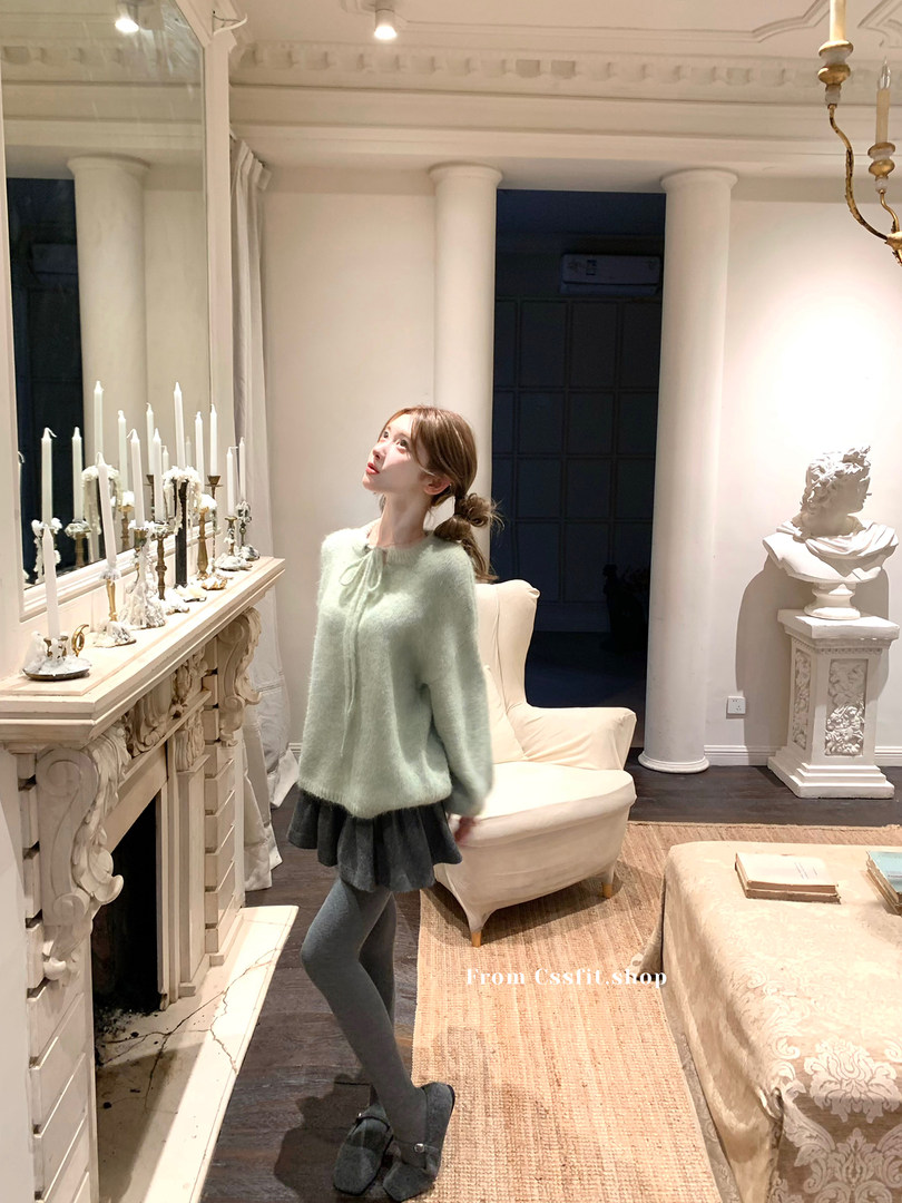 Model wearing a mint green fuzzy sweater with a dark skirt, tights, and black shoes indoors