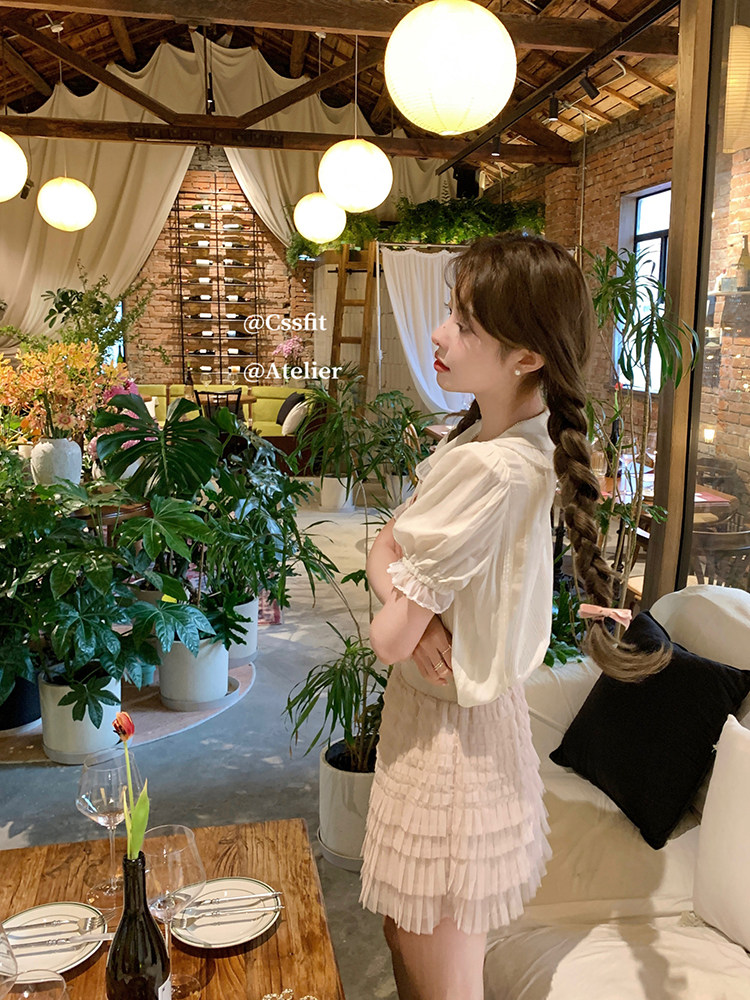 Woman wearing a white puff-sleeve top with a beige ruffled skirt in a stylish indoor setting