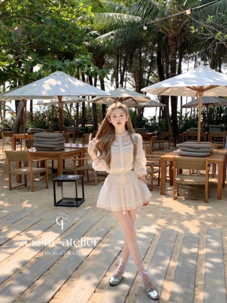 Model wearing a light cream long-sleeve dress with silver flats in a tropical beach setting