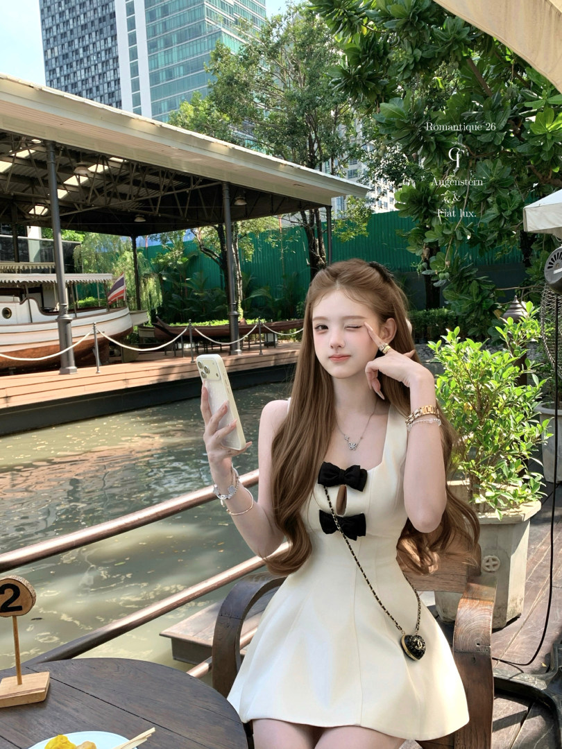 White sleeveless dress with black bow details worn by a model outdoors