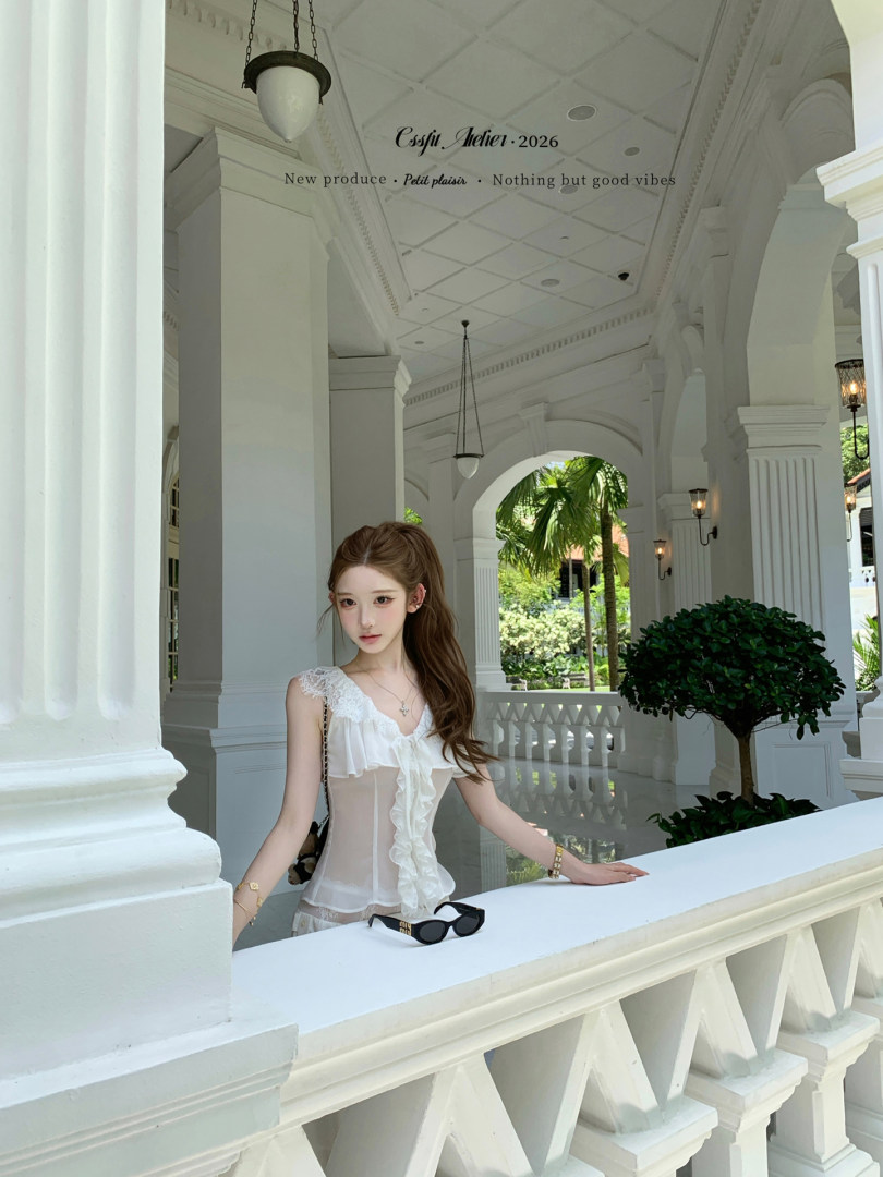 Woman wearing a white sheer ruffled top in a bright resort-style setting