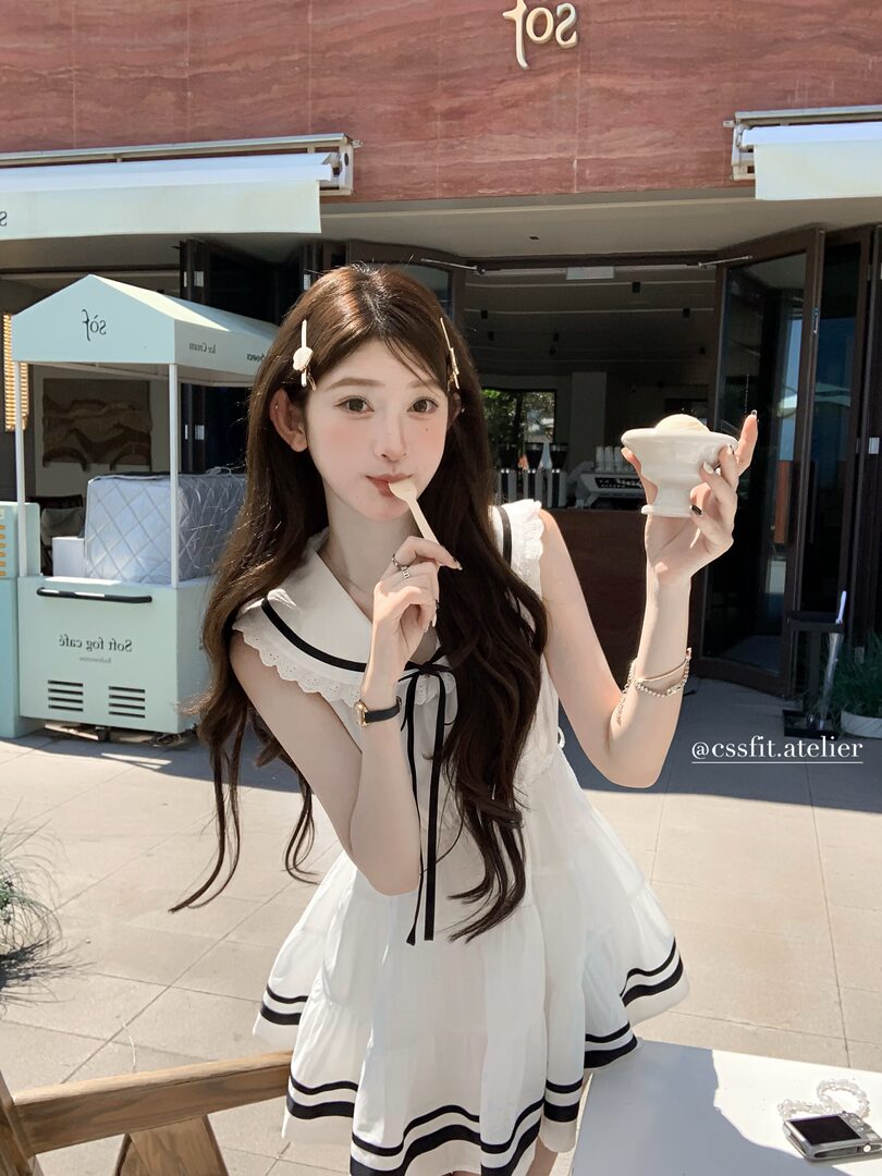 Woman wearing a white sailor-style sleeveless dress with black trim