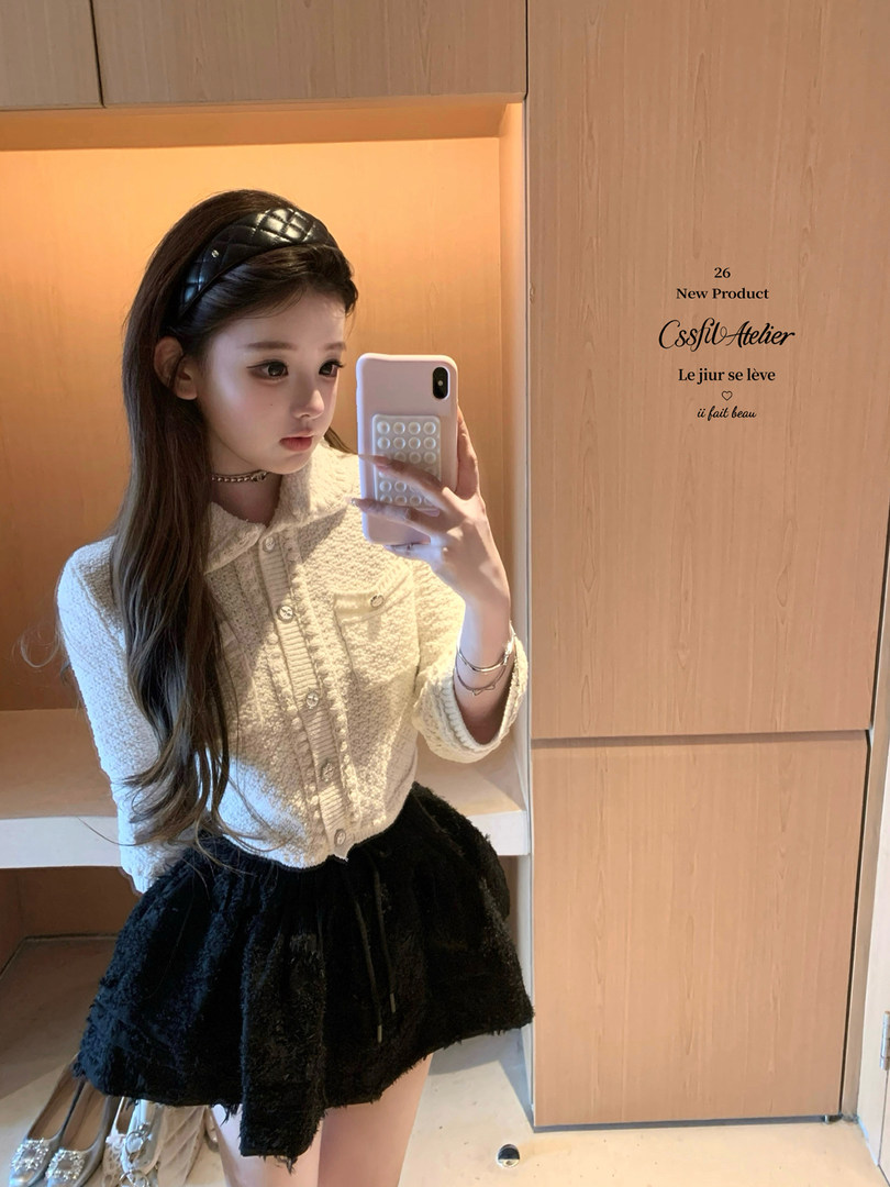 Mirror selfie of a woman wearing a cream textured cardigan and black skirt