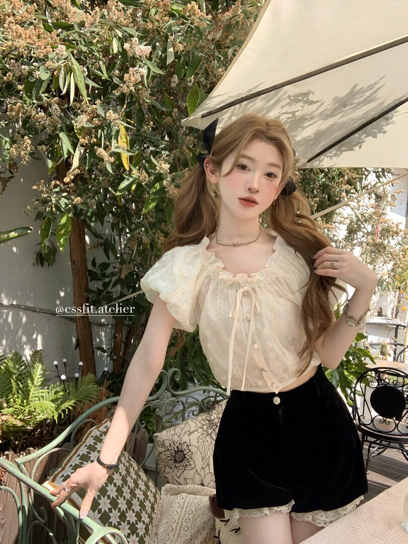 Woman wearing a cream ruffled blouse with black shorts outdoors