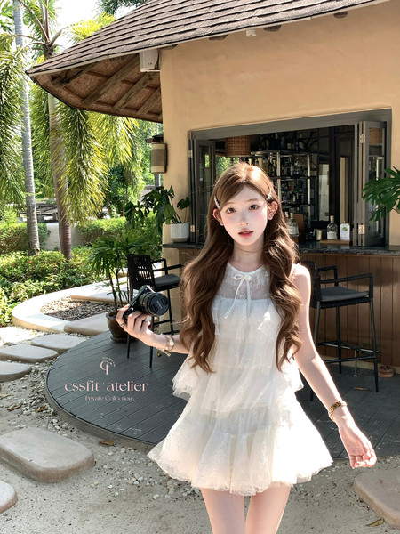 Woman wearing a white sleeveless ruffled dress outdoors in a tropical resort setting