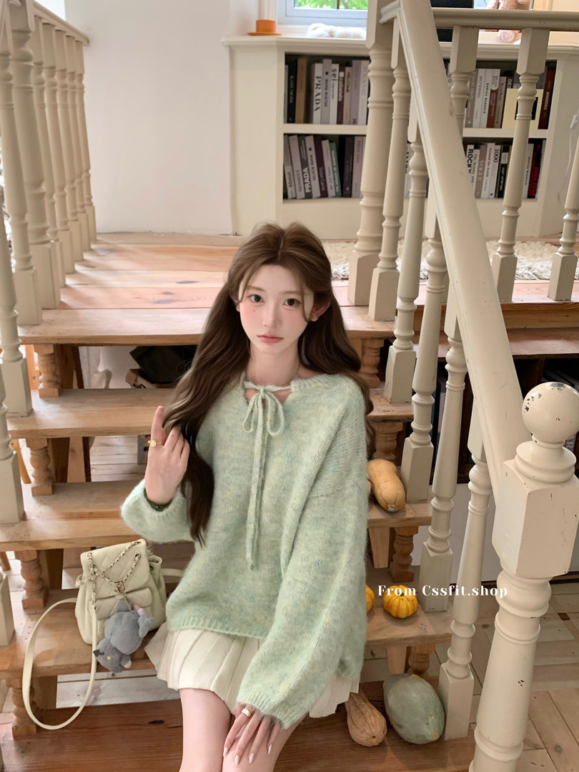 Model wearing a light mint fuzzy knit sweater with a bow tie detail and cream skirt on indoor stairs