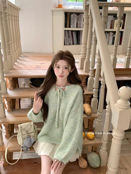 Model wearing a light mint fuzzy knit sweater with a bow tie detail and cream skirt on indoor stairs