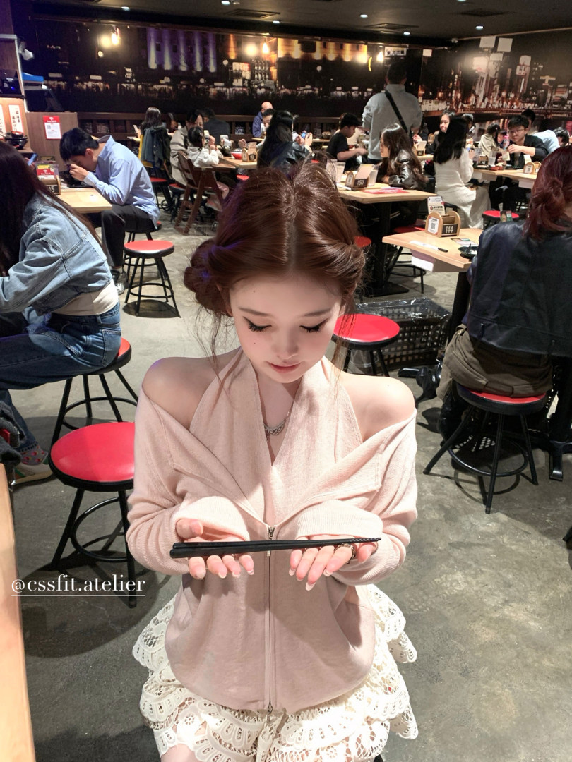 Woman wearing a light pink off-shoulder zip hoodie with lace-trimmed bottoms in a cafe