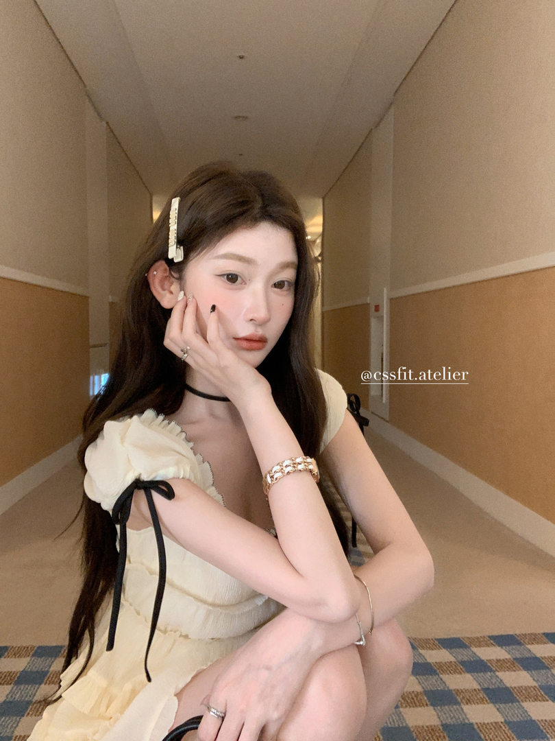 Model wearing a cream ribbon-trim dress with black bow details