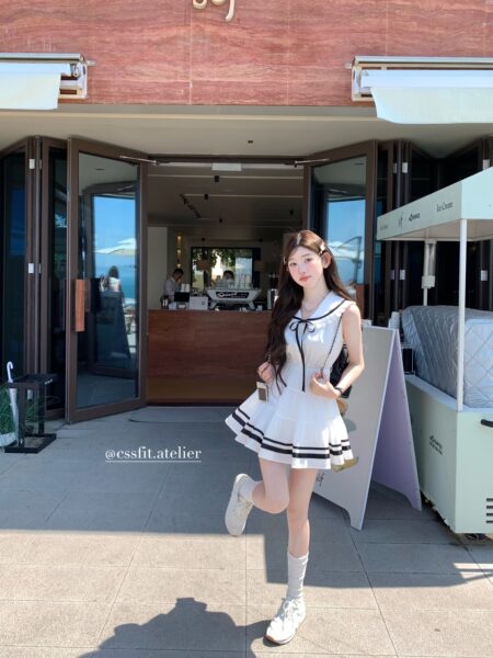 Woman wearing a white sleeveless ruffle dress with black trim and sneakers outdoors