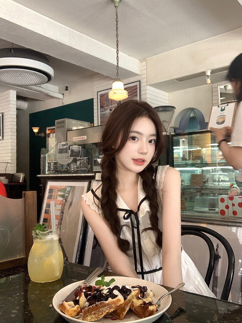 Young woman wearing a white sleeveless dress with black trim and a bow in a cafe