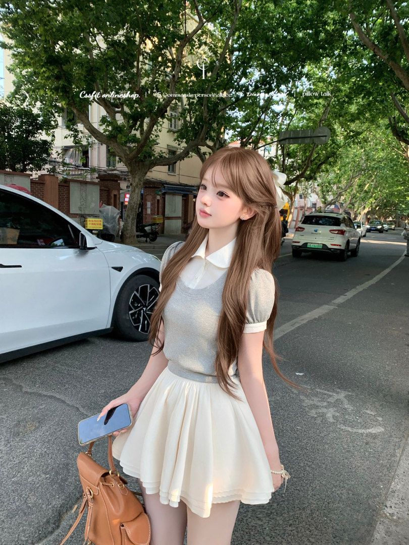 Woman wearing a gray top and cream skirt outdoors, holding a brown handbag