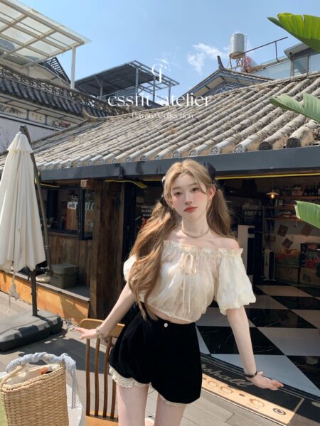 Woman wearing a cream off-shoulder blouse with black shorts outdoors