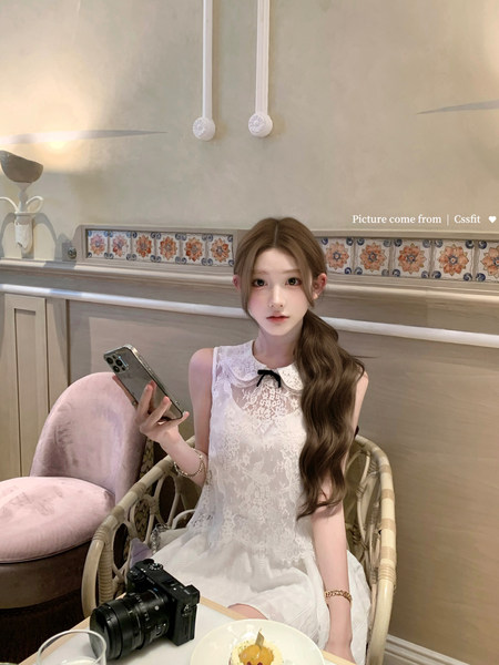 Woman wearing a white lace sleeveless dress while seated indoors