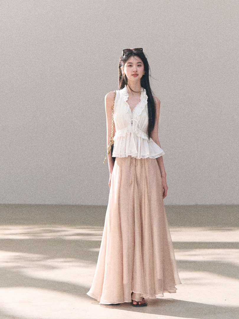 Model wearing a white lace sleeveless top with a flowing blush maxi skirt