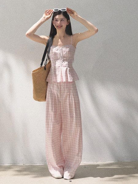 Model wearing a pink gingham two-piece outfit with a straw tote bag