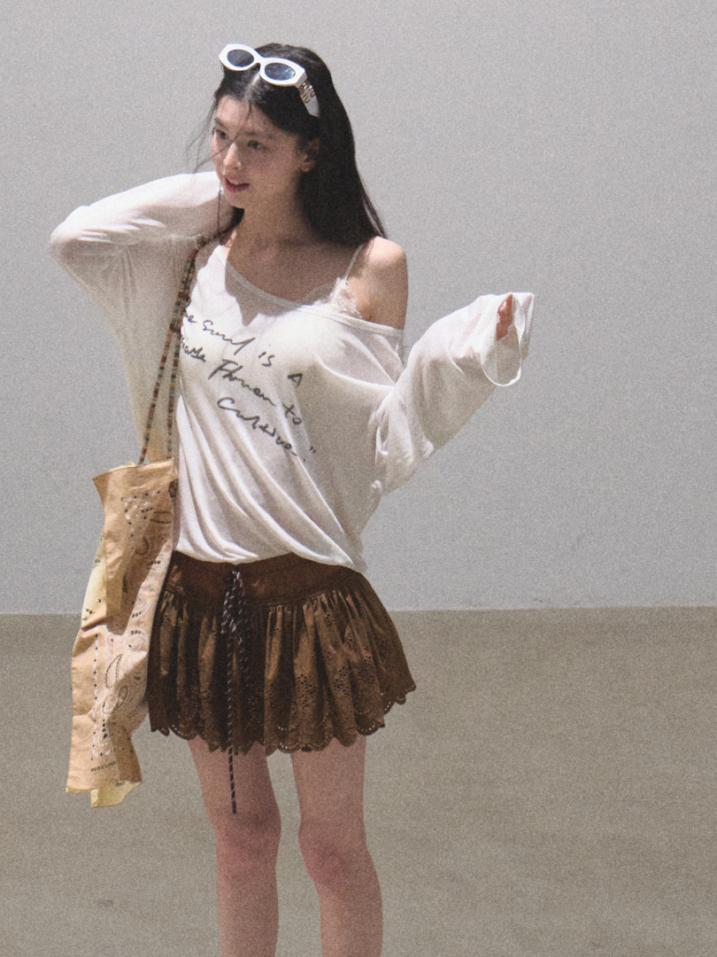 Woman wearing a white graphic off-shoulder top with a brown mini skirt and tote bag
